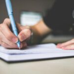 Trade Jobs That Pay Well 2026: Salary Guide, Apprenticeships & Career Paths Close-up of hand writing in notebook using a blue pen, focus on creativity.