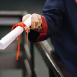 Chevening Scholarship 2025: Complete Guide to Winning (Selection Committee Insider Secrets) A close-up image of a graduate holding a diploma tied with a red ribbon, symbolizing achievement and success.