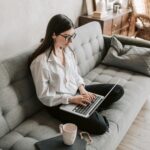 Woman in a cozy home setting working on a laptop for remote work and relaxation.