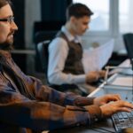 Two office workers focused on tasks at their desks in a modern workspace.