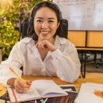 A cheerful businesswoman wearing a headset, working on documents in a modern office setting.