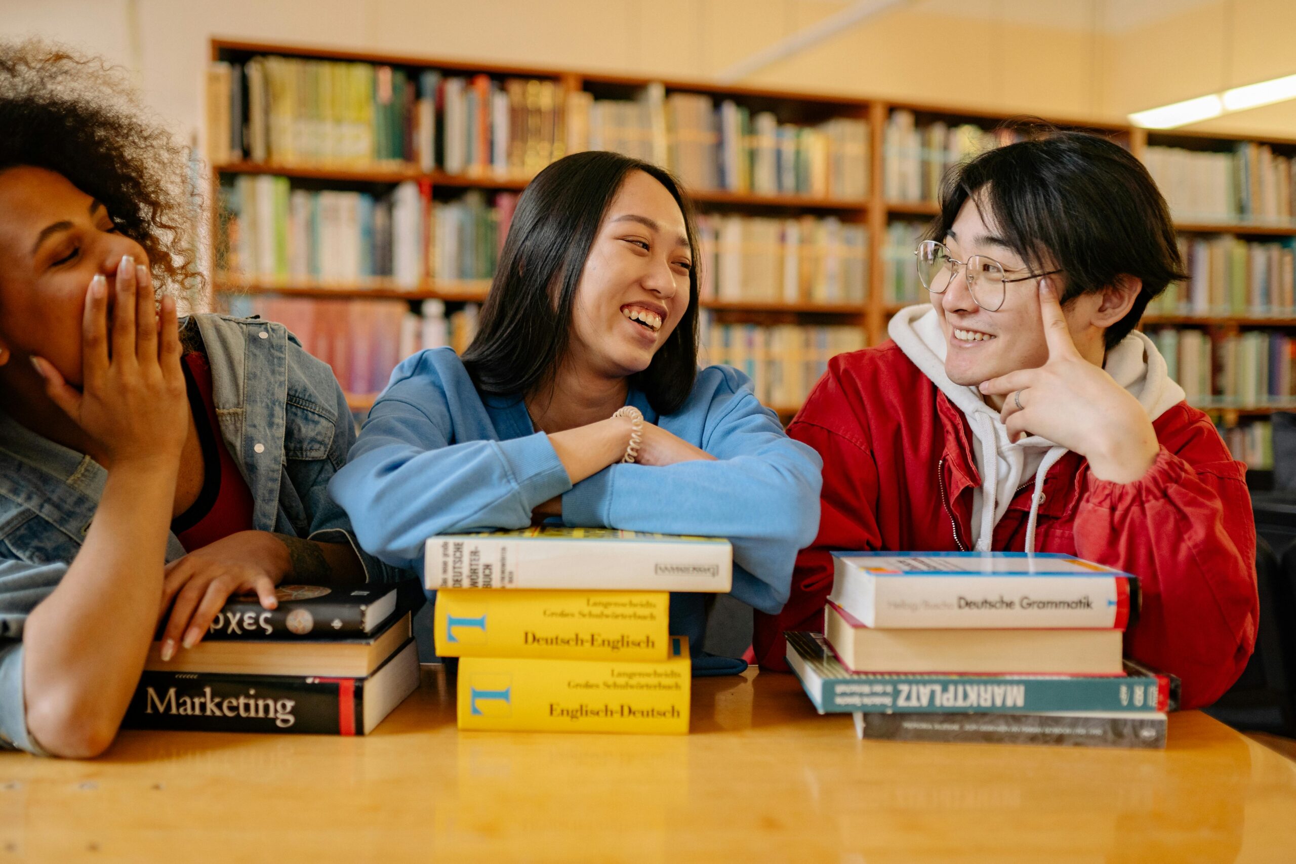 Three diverse students laughing and studying together in a cozy library setting.